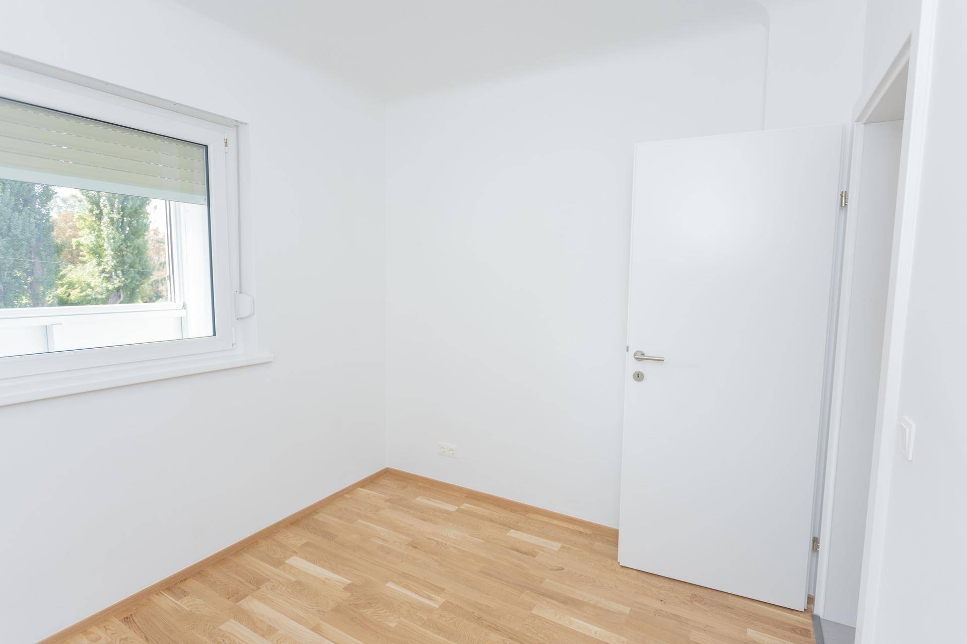Helles Zimmer mit Parkettboden und einem Fenster, das den Blick ins Grüne freigibt.