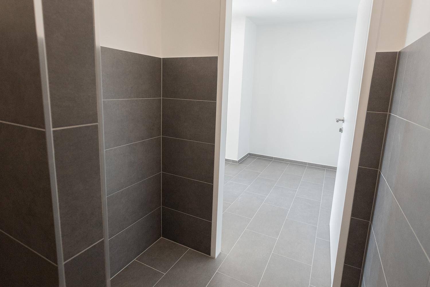 Blick aus einem gefliesten Raum in einen hellen Flur mit modernen Bodenfliesen.