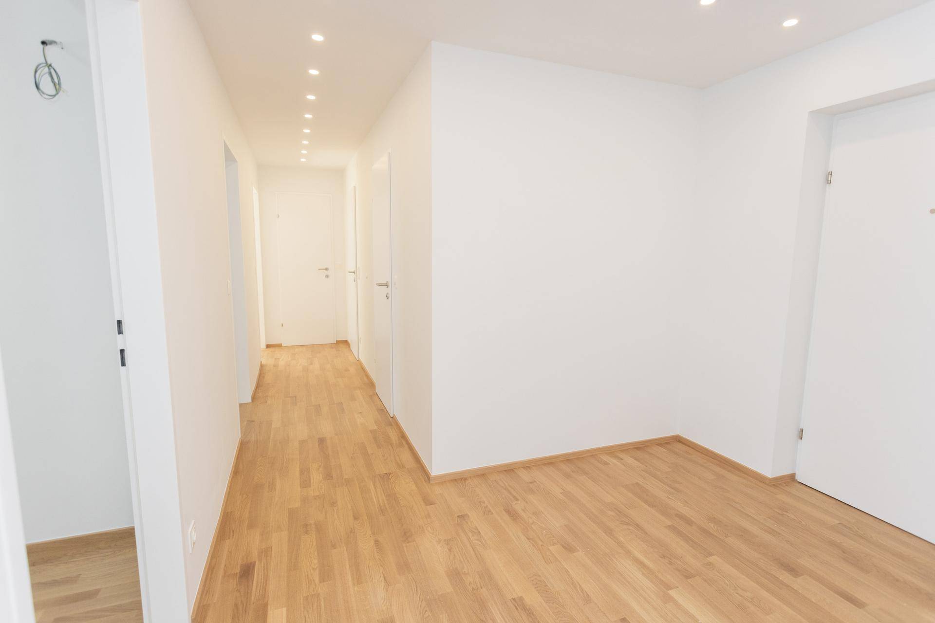 Langer, heller Flur mit Holzboden und mehreren Türen zu den Zimmern, modern gestaltet.