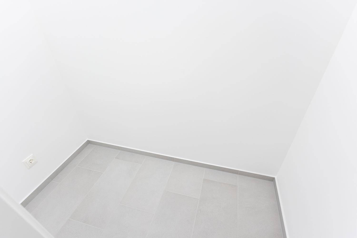 Leerer Raum mit grauen Fliesen und weißen Wänden, bereit für individuelle Gestaltung.