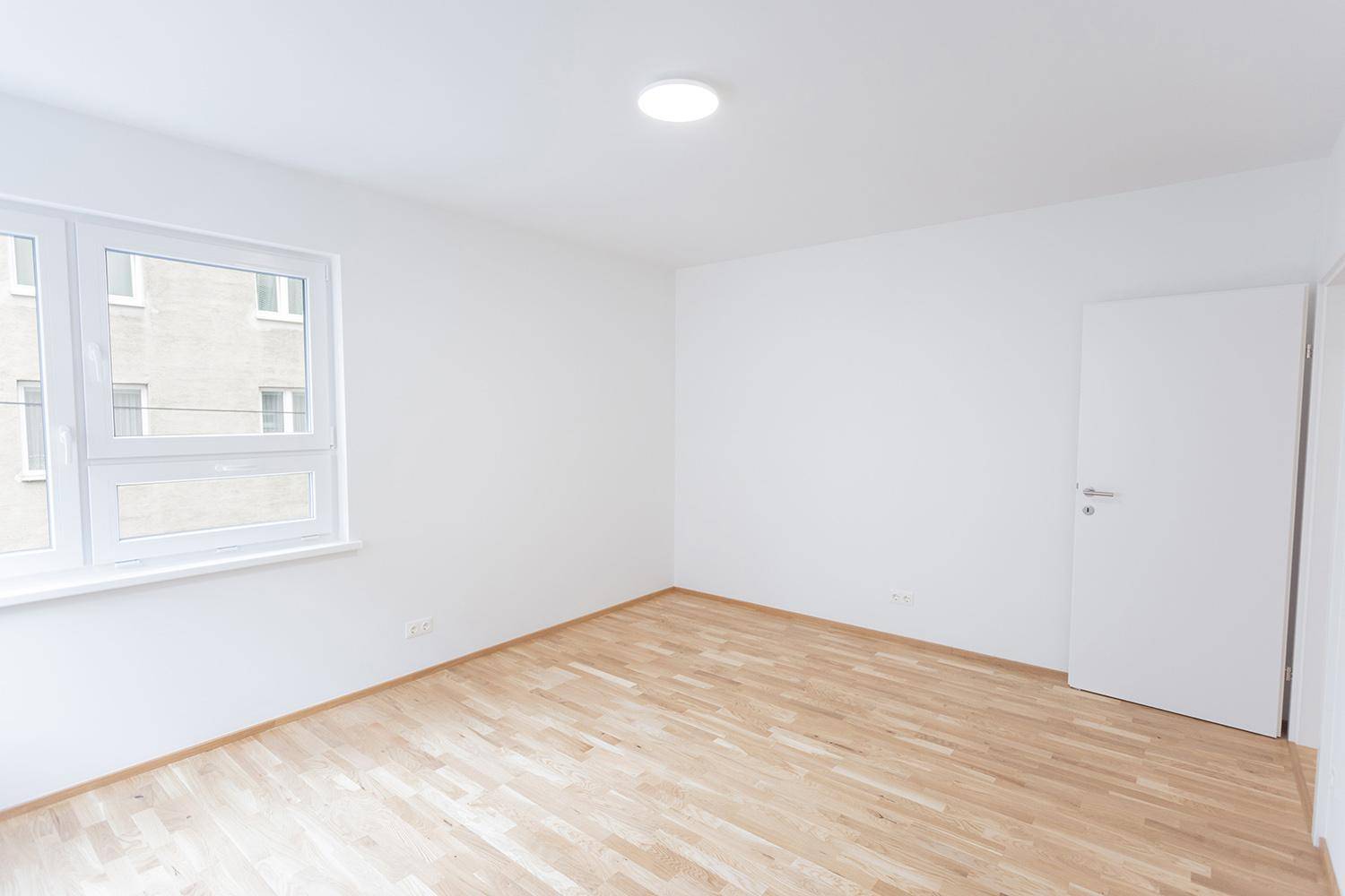 Leeres Schlafzimmer mit Holzparkettboden und großen Fenstern, das viel Licht bietet.