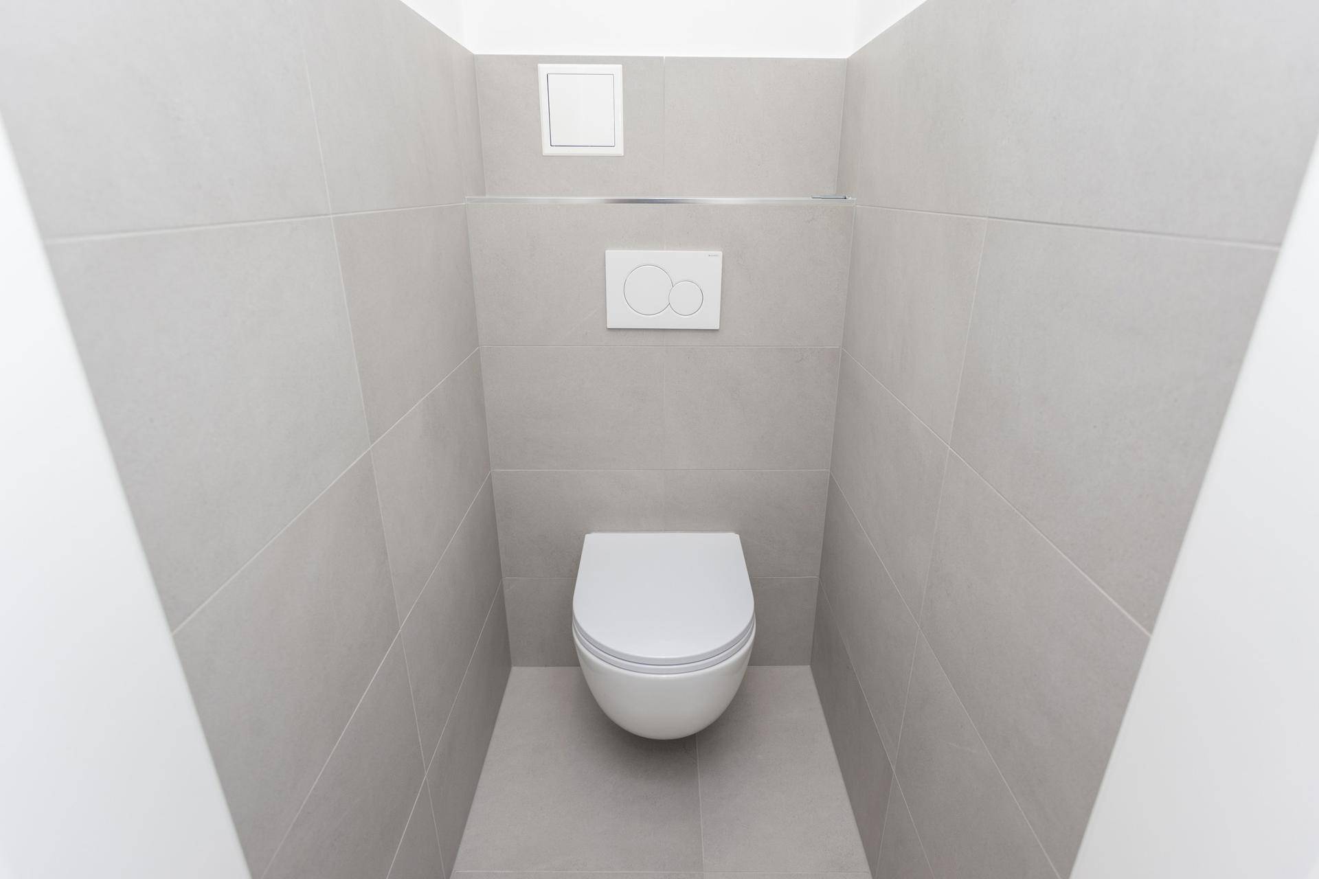 Separates WC mit modernen grauen Fliesen und wandhängender Toilette.