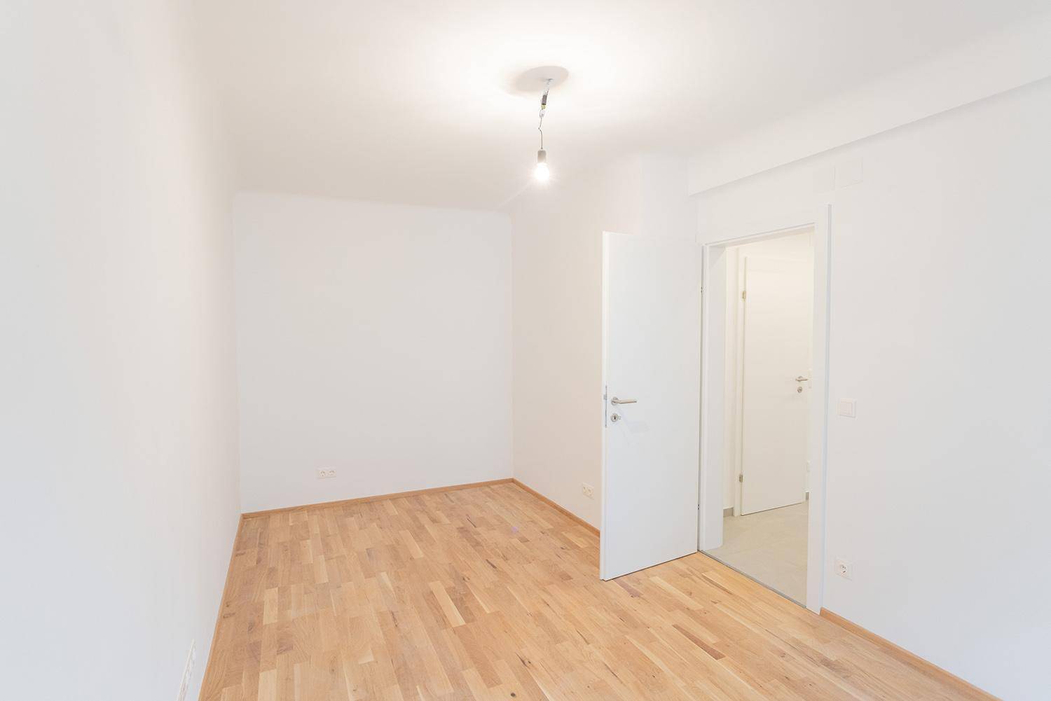 Leeres Zimmer mit hellem Parkettboden und weiß gestrichenen Wänden, bereit zur individuellen Gestaltung.