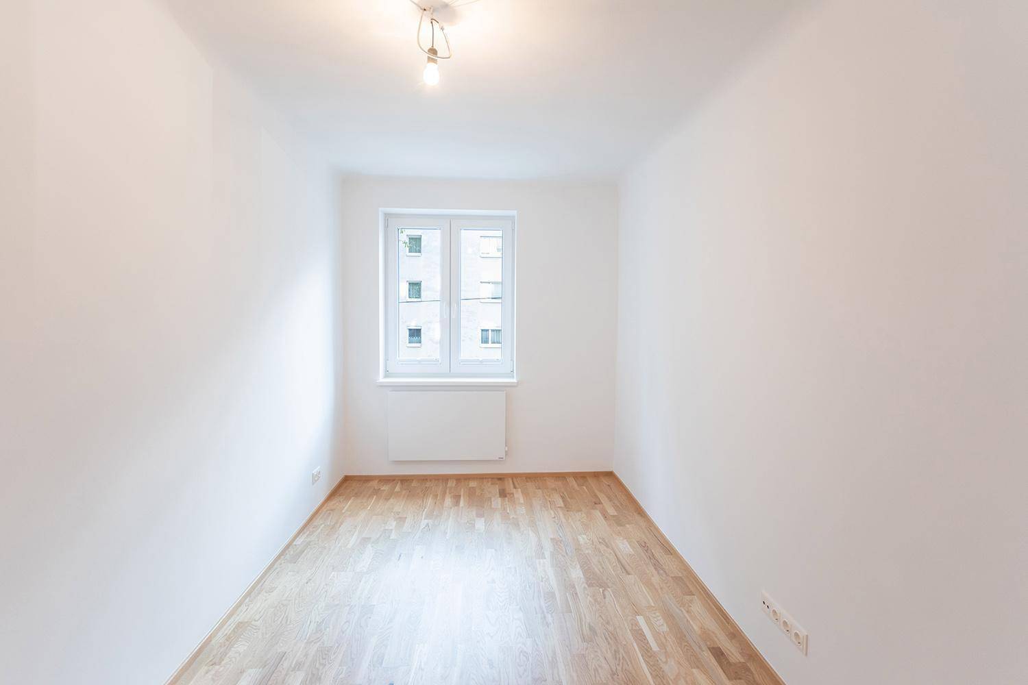 Helles, leeres Schlafzimmer mit Parkettboden und einem Fenster.