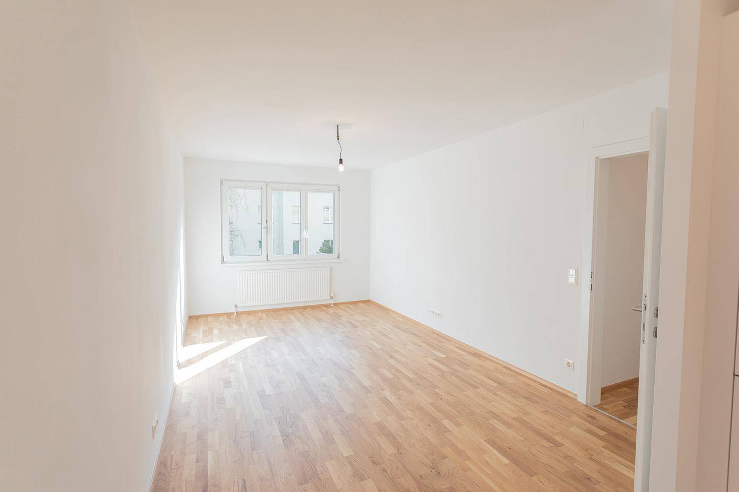 Heller, leerer Raum mit Parkettboden und Fenster, das für eine angenehme Atmosphäre sorgt.