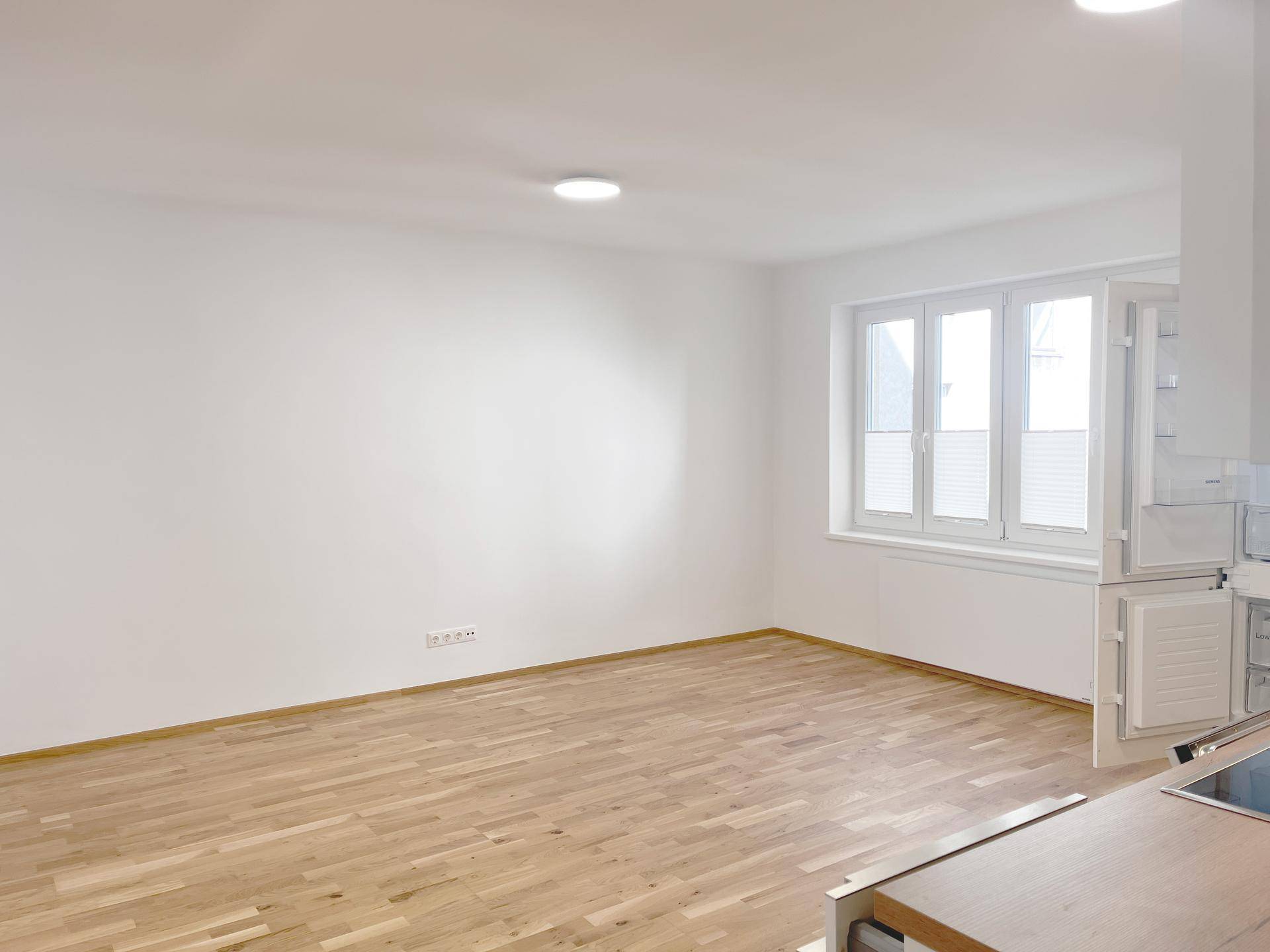 Heller, leerer Wohnbereich mit Parkettboden und großen Fenstern.