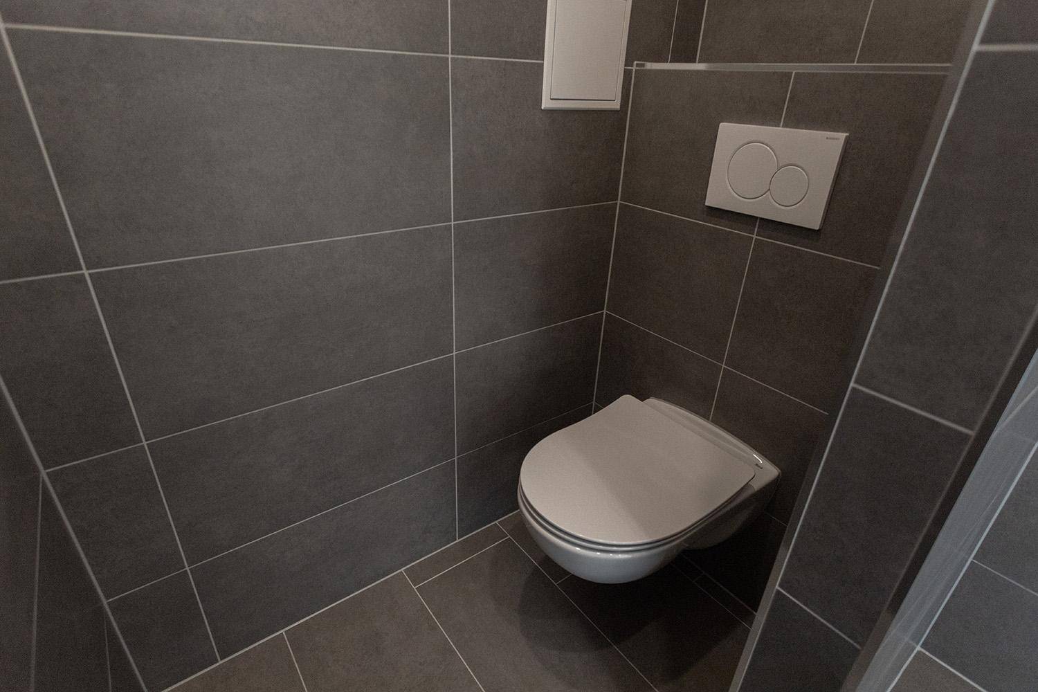 Modernes Gäste-WC mit dunklen Fliesen und wandhängendem WC für ein sauberes Design.