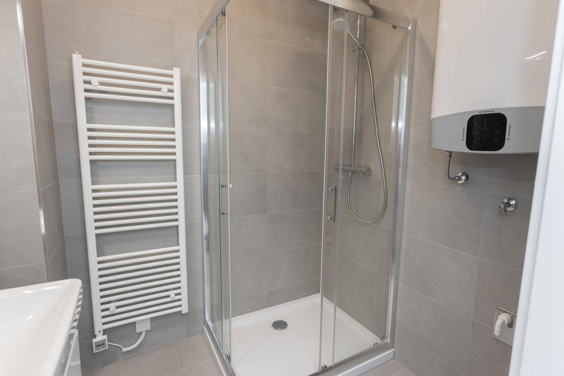 Modernes Duschbad mit Glasduschkabine, beheiztem Handtuchhalter und grauen Fliesen.
