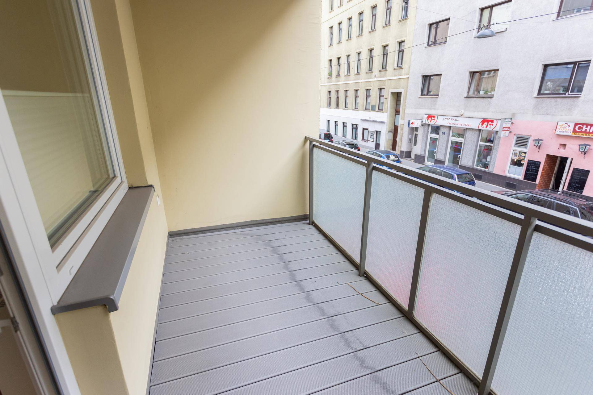 Kleiner Balkon mit modernem Bodenbelag und Blick auf die städtische Umgebung.