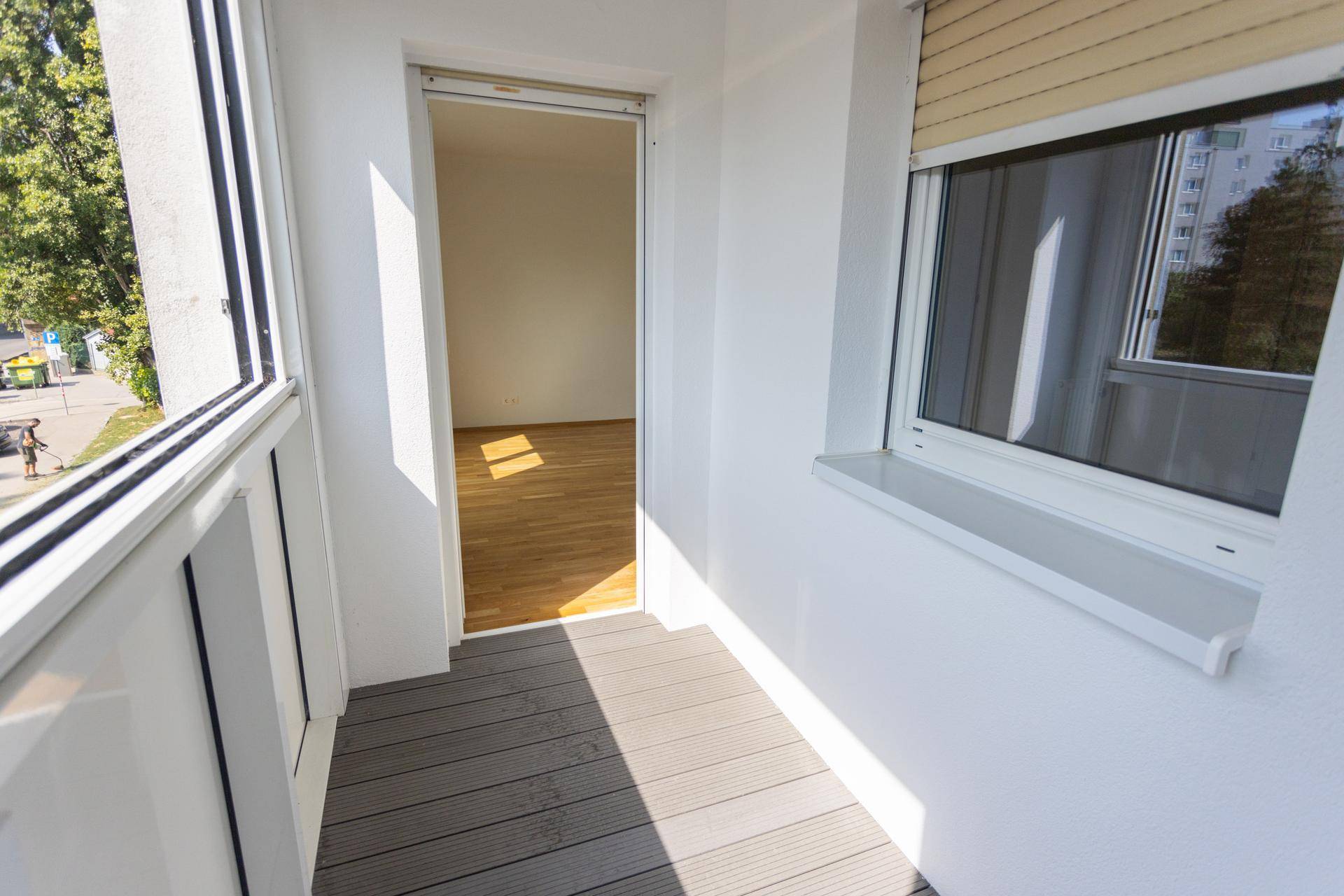 Heller Balkon mit Holzdielenboden und Zugang zu einem Innenraum mit Parkett.
