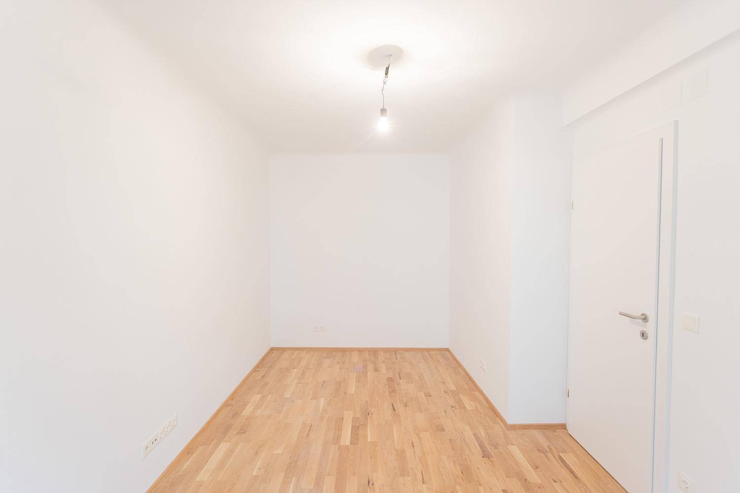 Unmöbliertes Zimmer mit Holzboden und weißer Tür, bietet vielseitige Nutzungsmöglichkeiten.