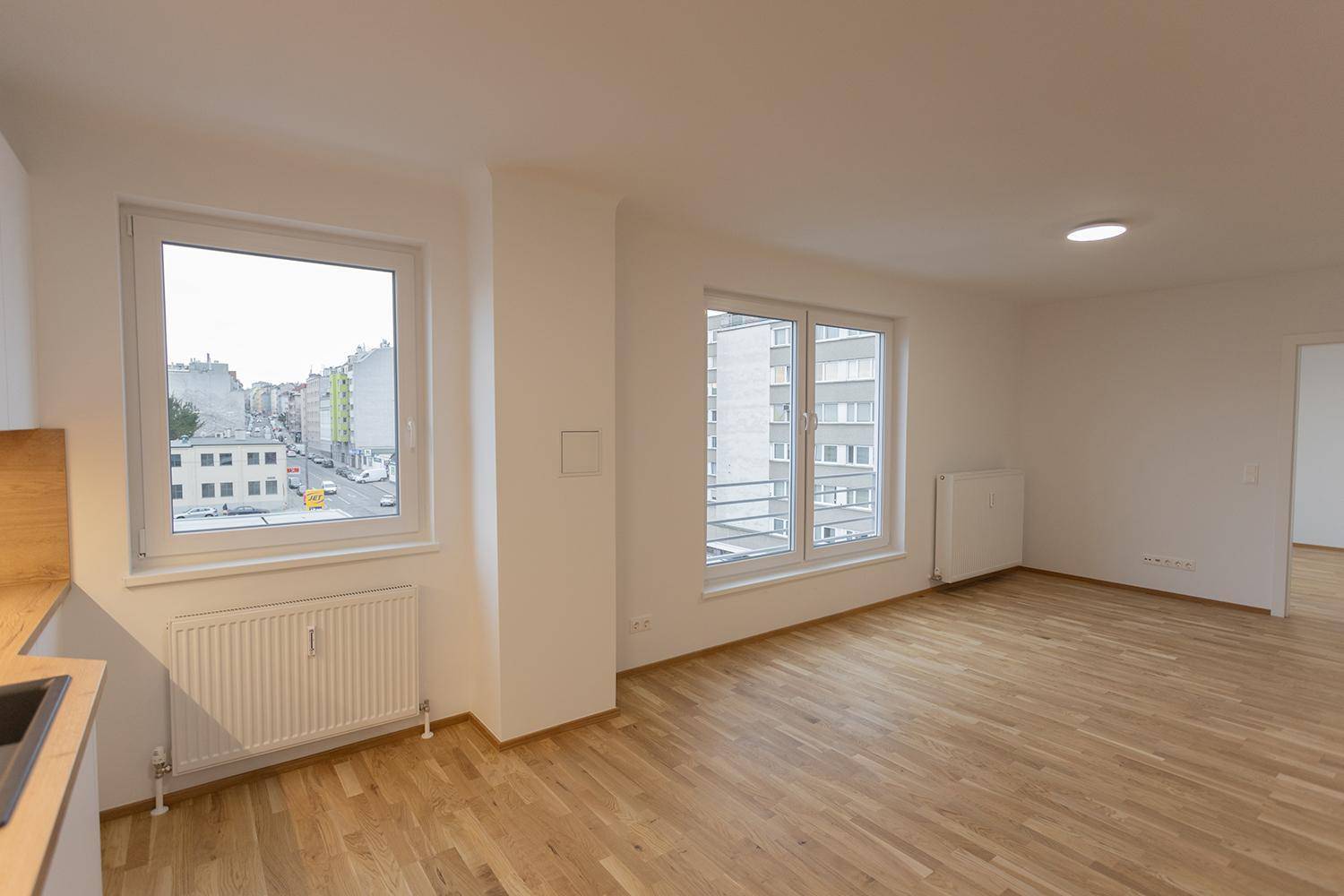 Lichtdurchfluteter Raum mit Holzboden und Fenstern mit Blick auf die Straße.