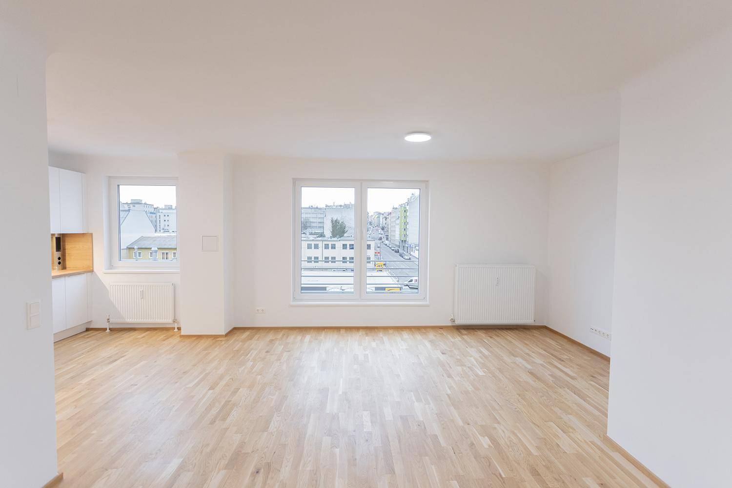 Heller Raum mit Holzboden und mehreren Fenstern, die einen Stadtblick bieten.