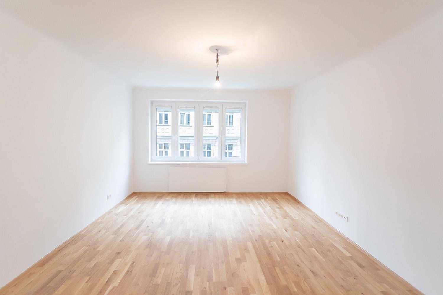 Heller, leerer Raum mit Parkettboden und großen Fenstern, ideal als Wohnzimmer.