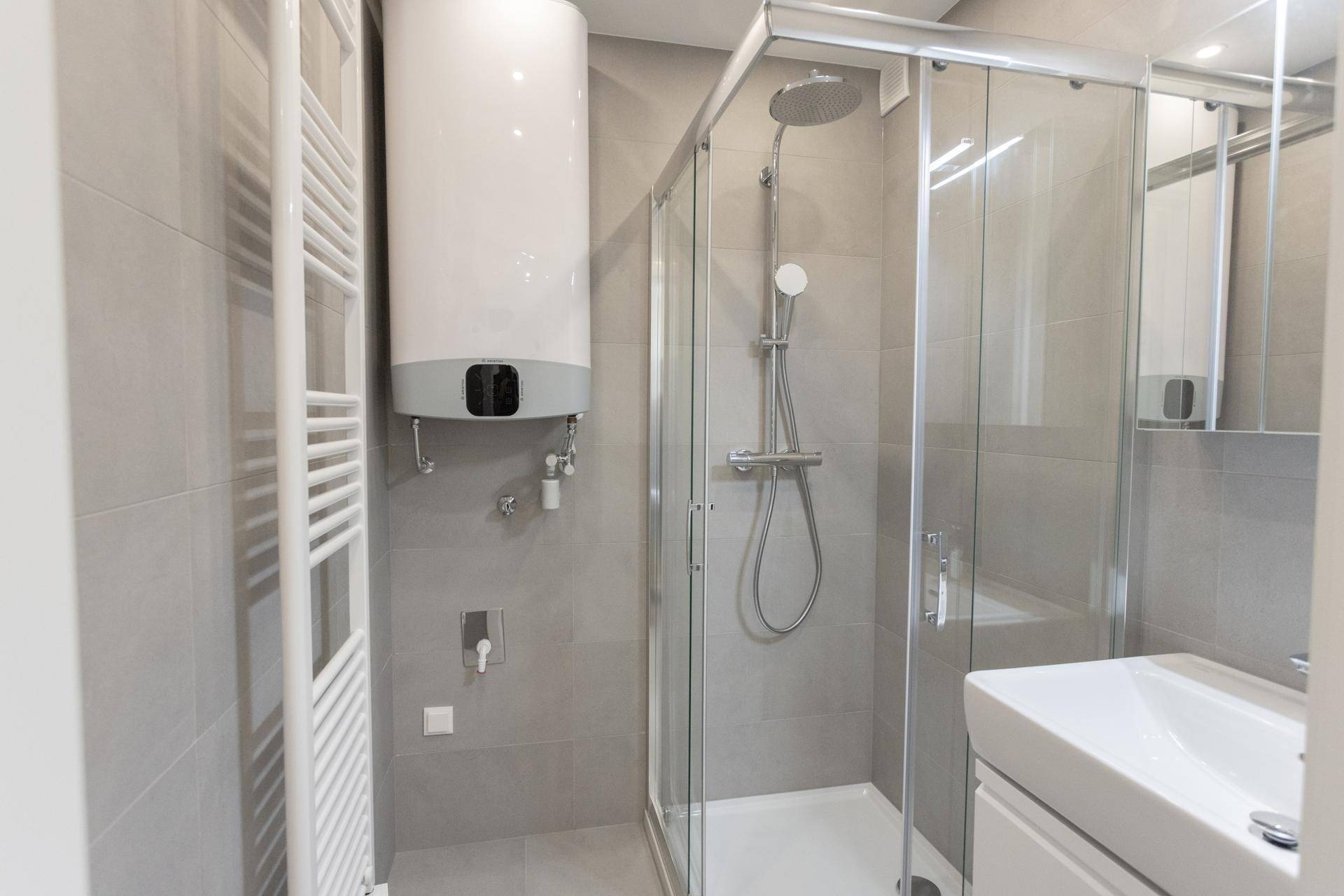 Modernes Badezimmer mit grauen Fliesen, Duschkabine, Waschbecken und beheiztem Handtuchhalter.