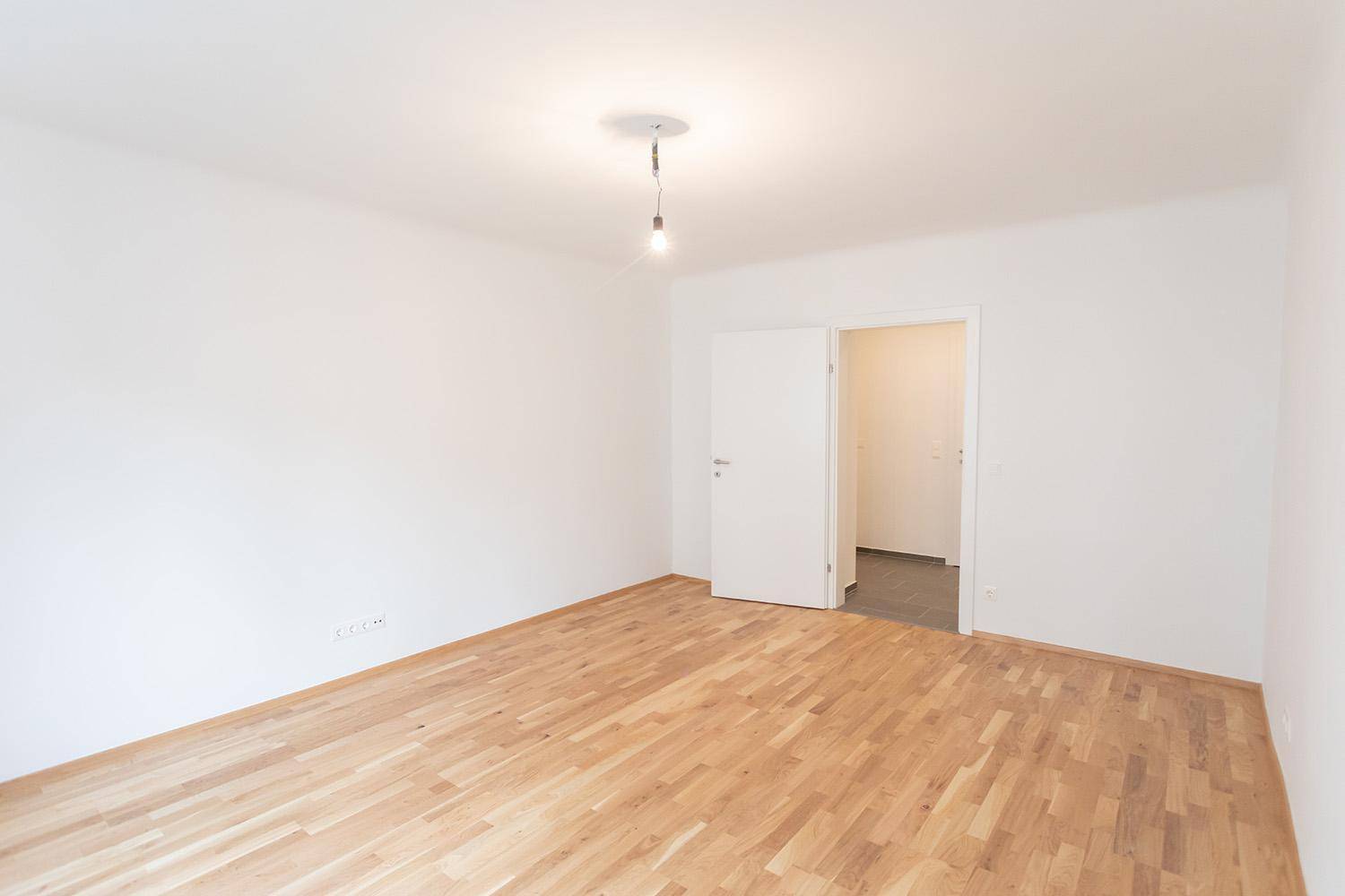 Leeres Zimmer mit hellem Parkettboden und Zugang zum Flur.