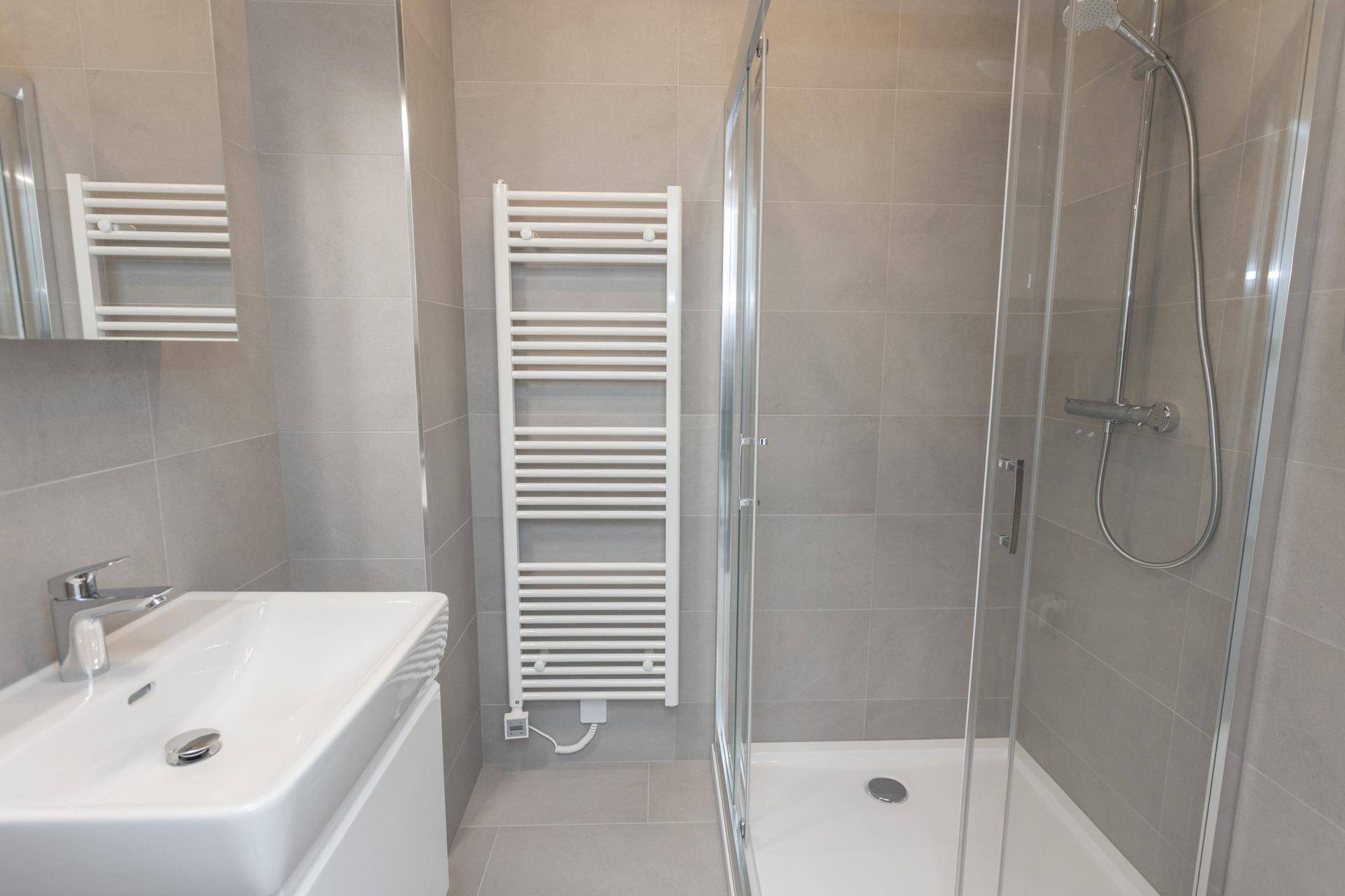 Helles Badezimmer mit modernem Waschbecken, Spiegel, Duschkabine und Handtuchheizkörper.