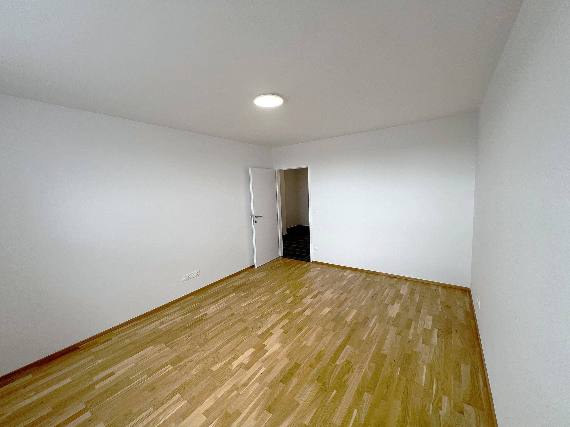 Leeres Zimmer mit hellem Parkettboden und weiß gestrichenen Wänden, bereit zur Einrichtung.