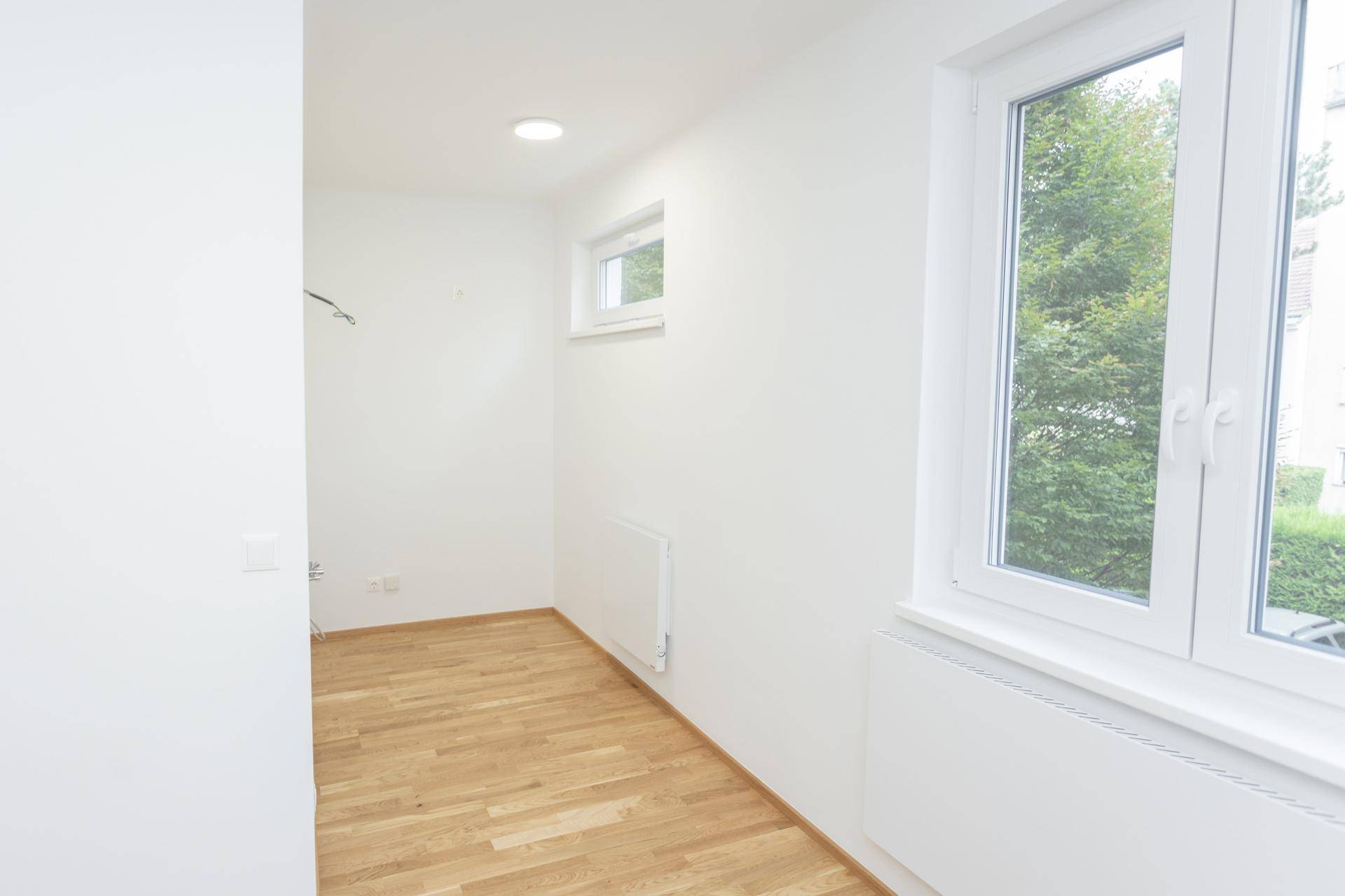 Heller Raum mit Holzboden und Blick ins Grüne durch das große Fenster.