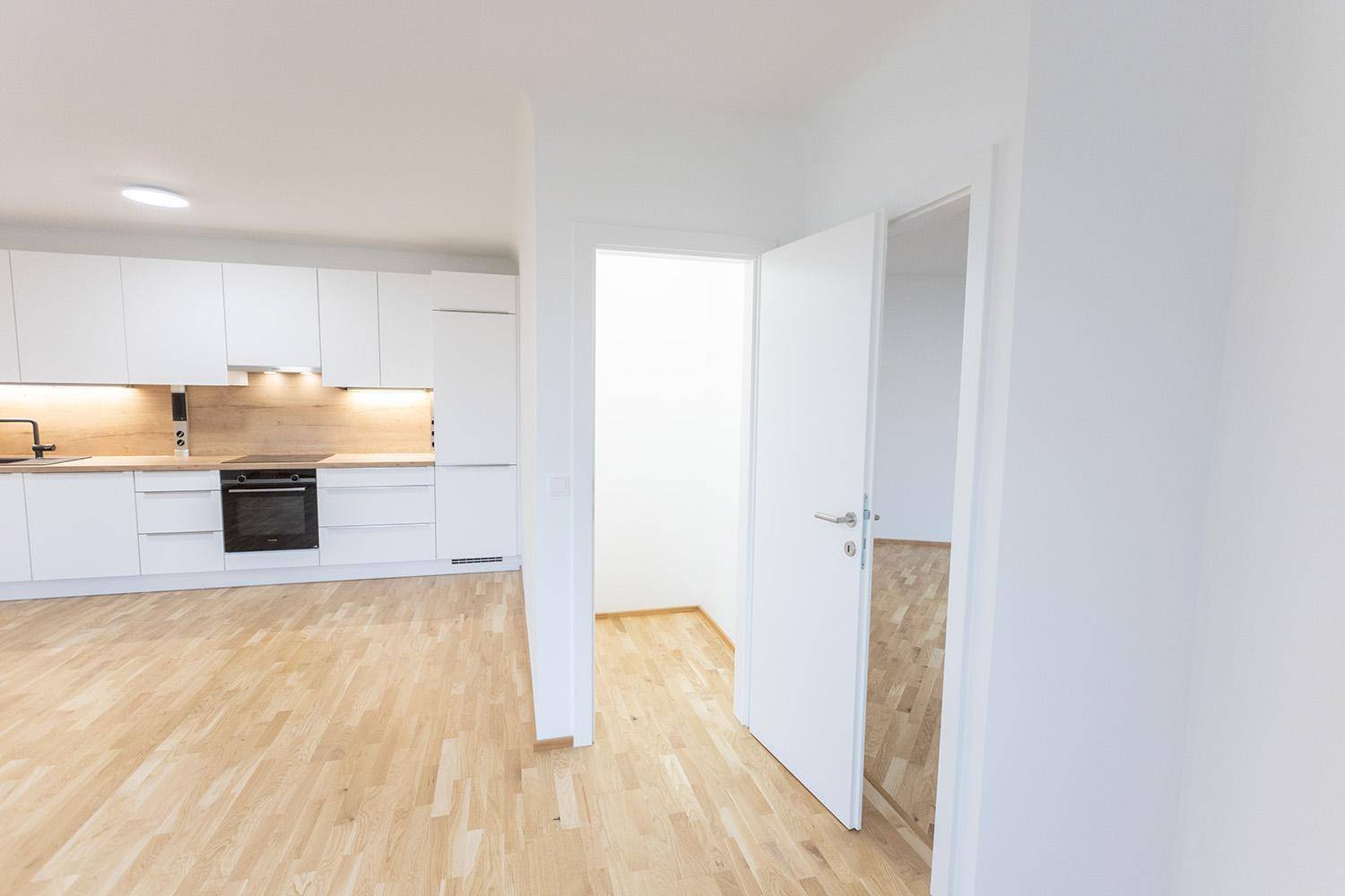 Helle, offene Wohnküche mit modernen weißen Schränken und Holzboden, bereit zur Einrichtung.
