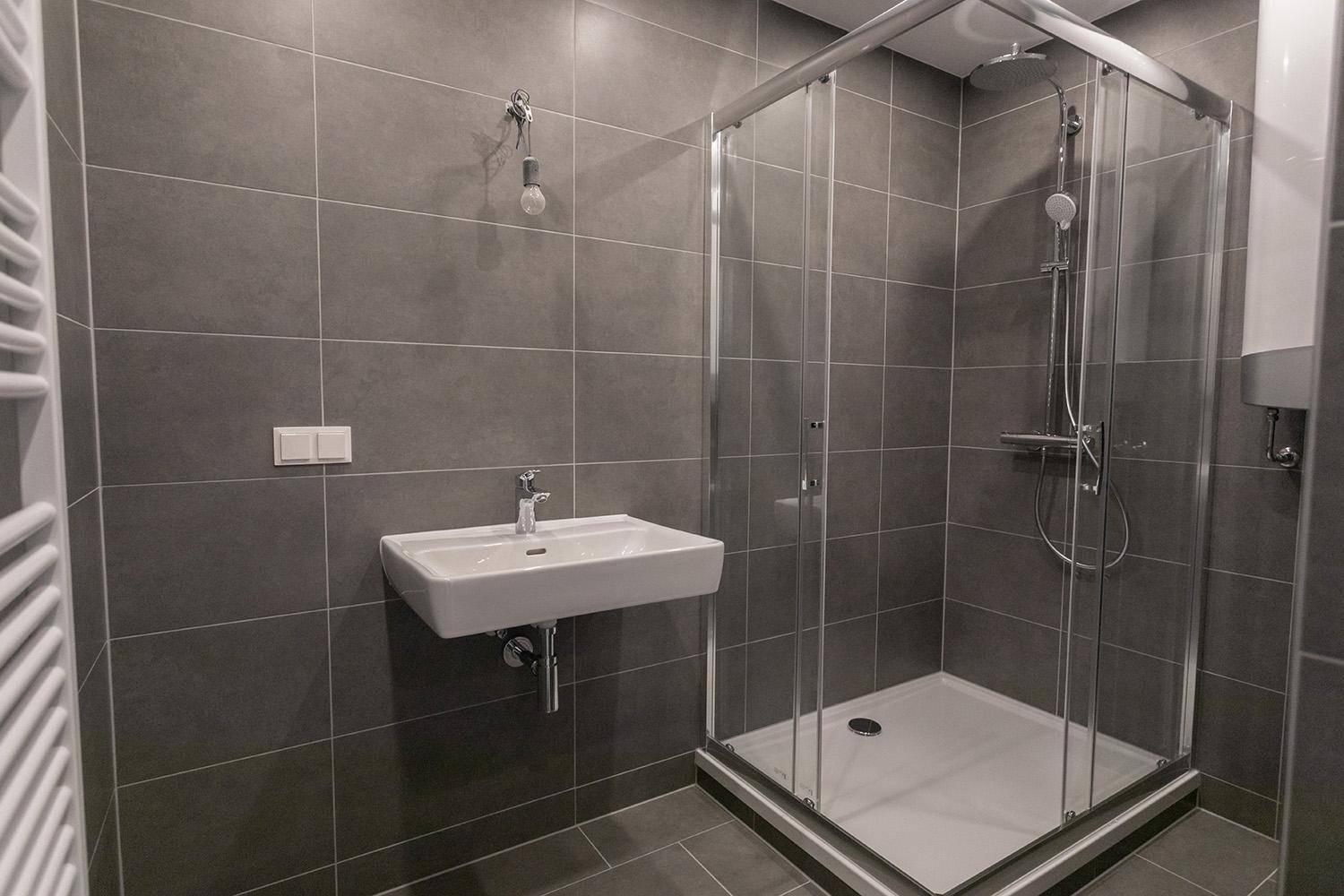 Modernes Badezimmer mit Duschkabine, Waschbecken und grauen Fliesen, gut beleuchtet und geräumig.