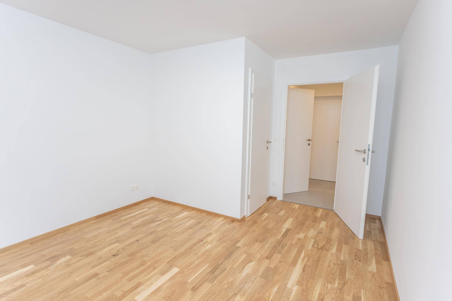 Heller, leerer Raum mit Parkettboden und mehreren Türen zu angrenzenden Zimmern.