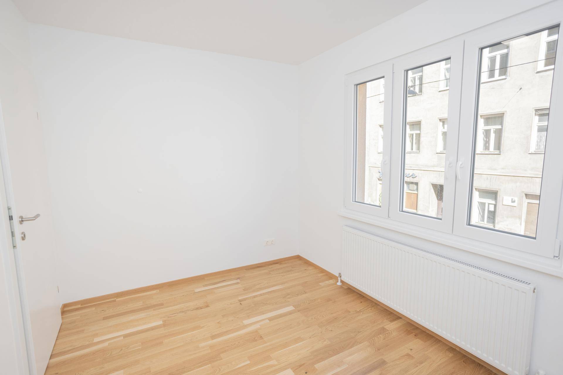 Helles Zimmer mit Parkettboden und großen Fenstern, die viel natürliches Licht hereinlassen.