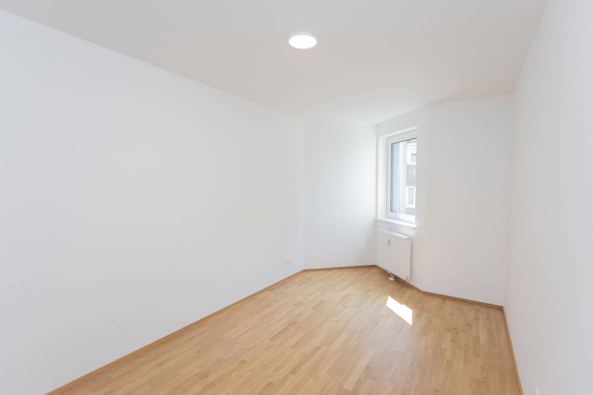 Leeres Zimmer mit hellem Parkettboden und weiß gestrichenen Wänden, vielseitig nutzbar.