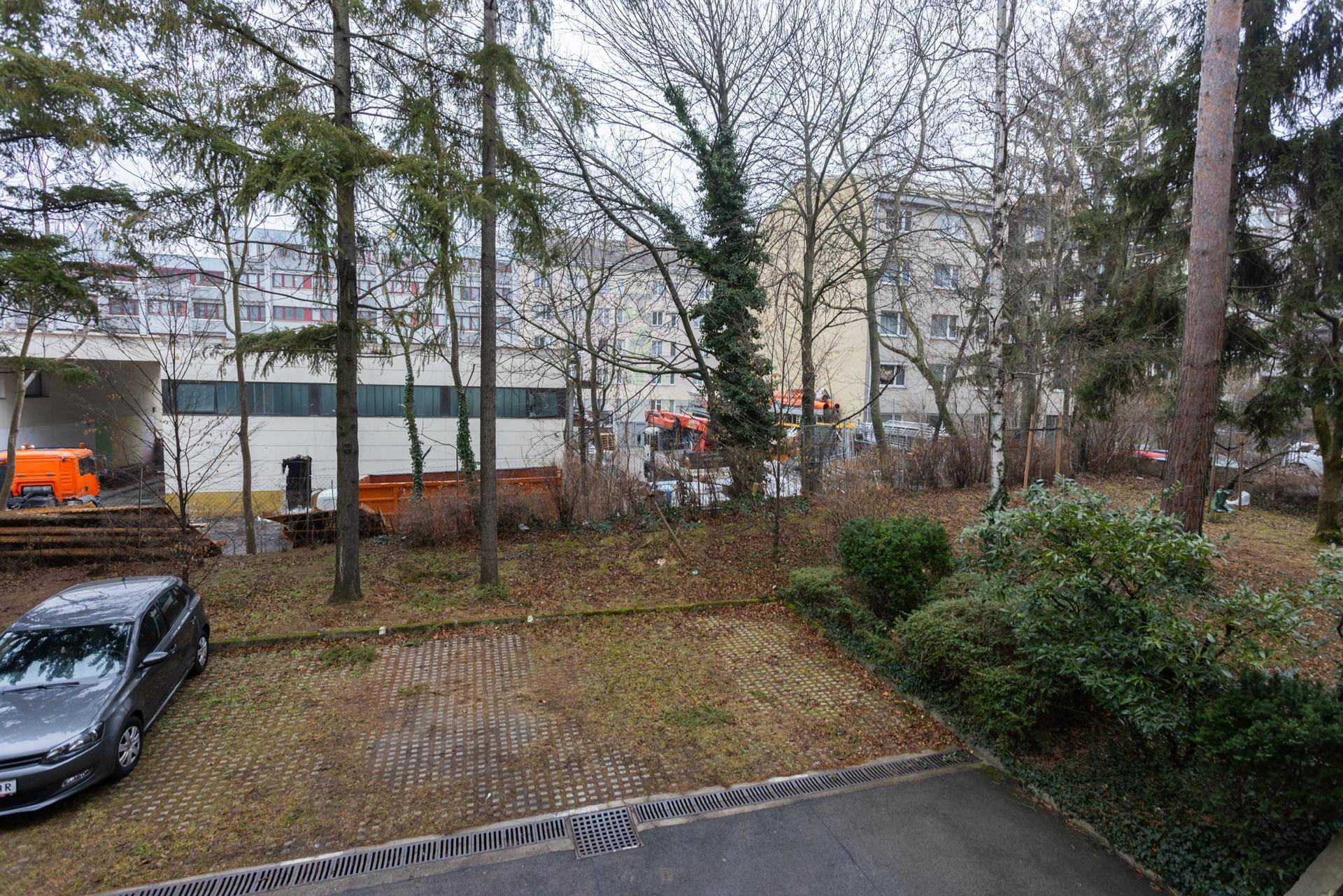 Blick aus dem Fenster auf einen Parkplatz, Bäume und umliegende Gebäude.