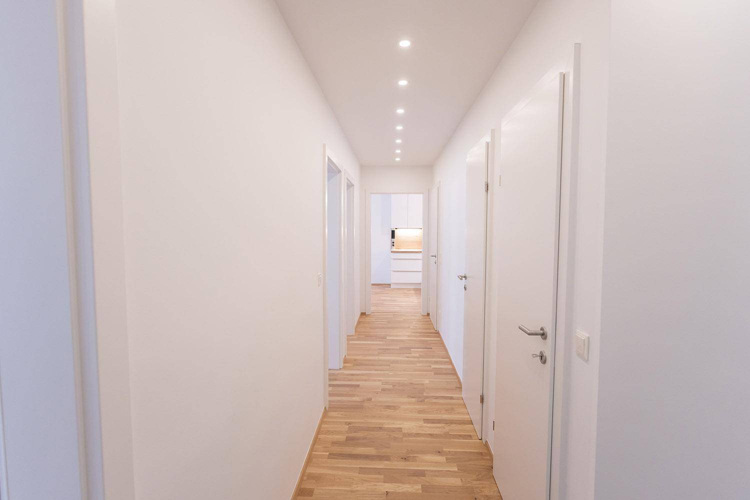 Langer, heller Flur mit Holzboden und Einbaustrahlern, der zu weiteren Räumen führt.