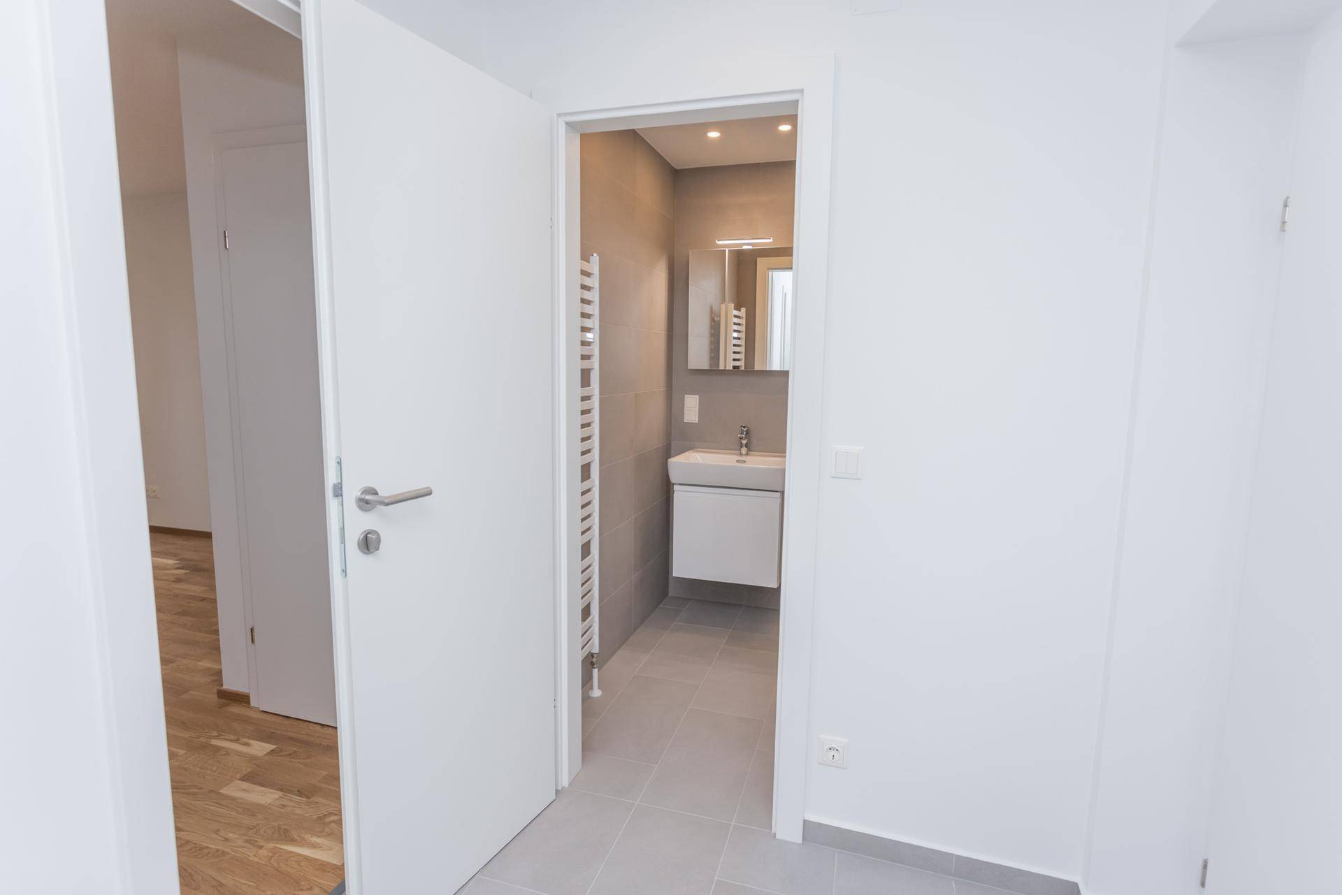 Heller Flur mit Blick in ein modernes Badezimmer mit Dusche.