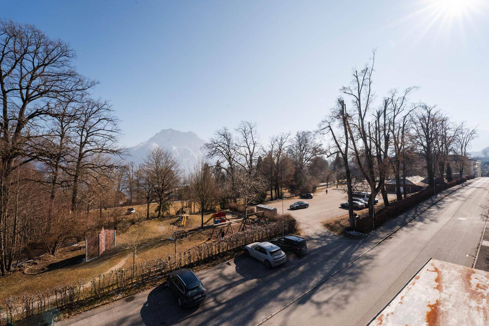 Weitläufiger Blick über einen Spielplatz, Bäume und Berge unter strahlendem Himmel.