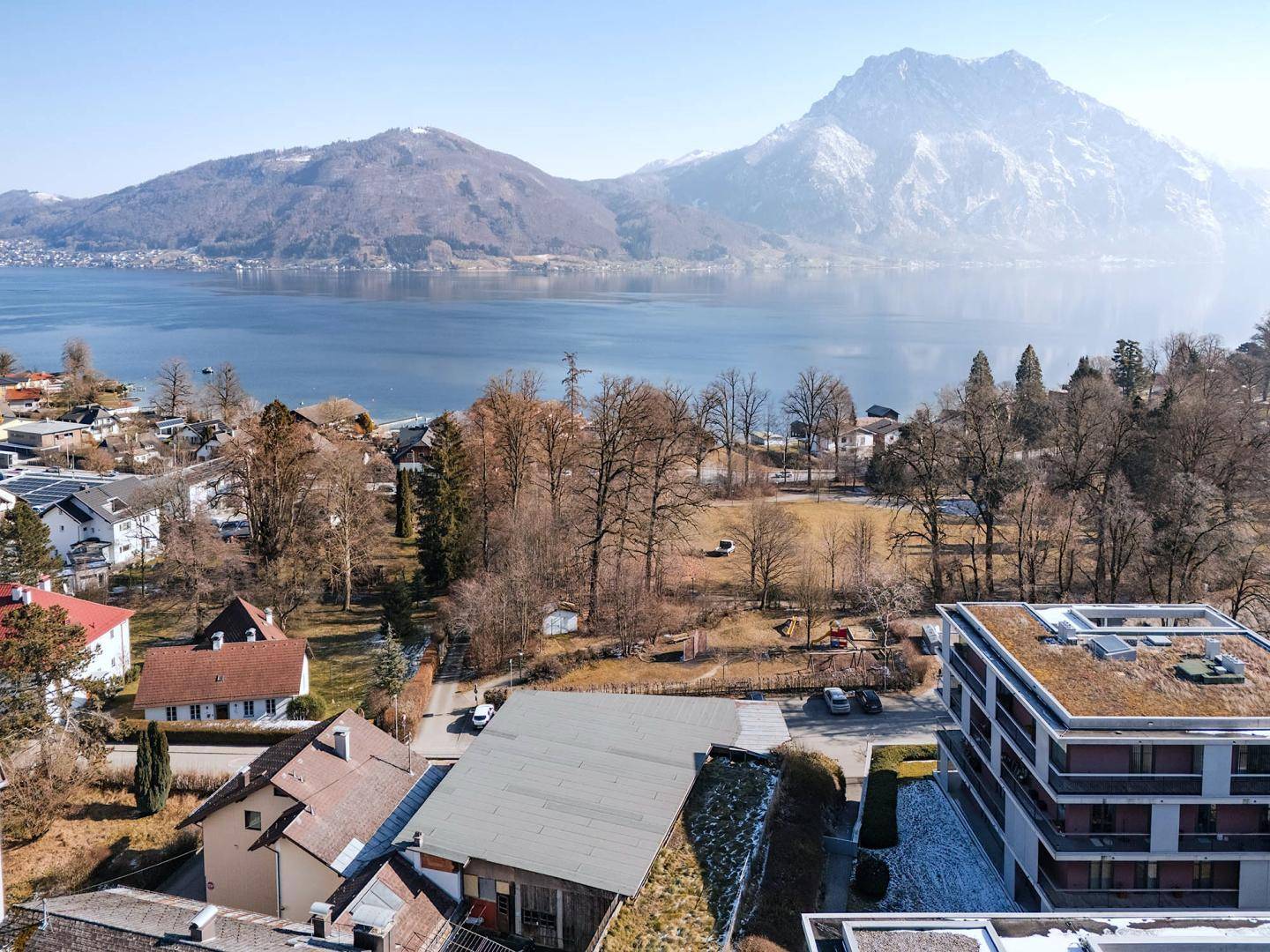 Weitläufige Aussicht auf den See, schneebedeckte Berge und eine Wohnsiedlung.