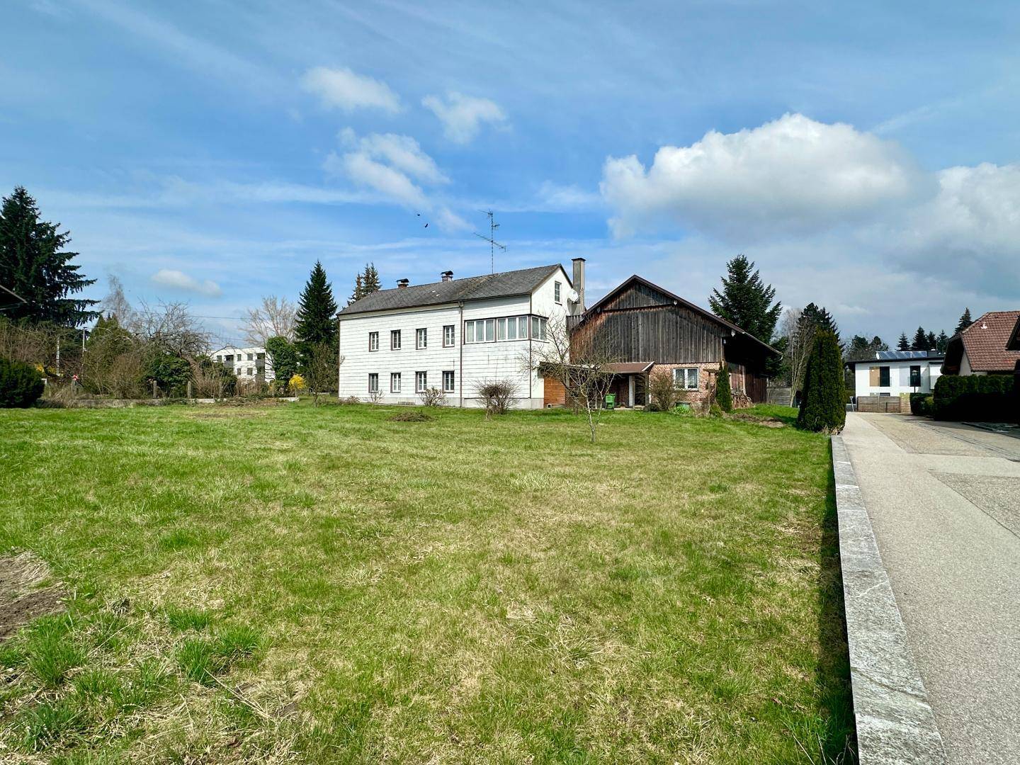 Offenes grünes Grundstück mit angrenzender Straße und verschiedenen Wohnhäusern im Hintergrund.