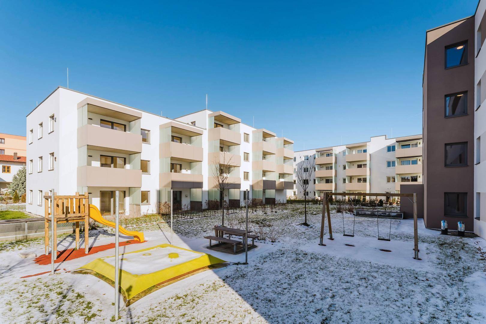Gemeinschaftlicher Gartenbereich mit Spielplatz und Sitzgelegenheiten, umgeben von modernen Wohngebäuden.