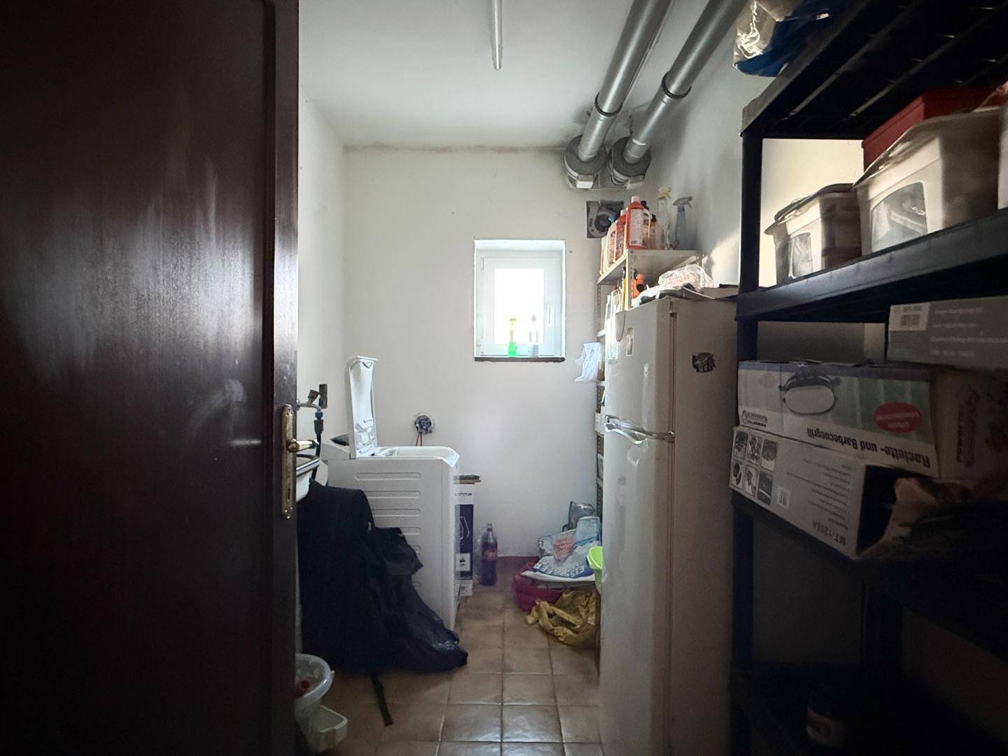 Praktischer Hauswirtschaftsraum mit Waschmaschine, Kühlschrank und Regalen.