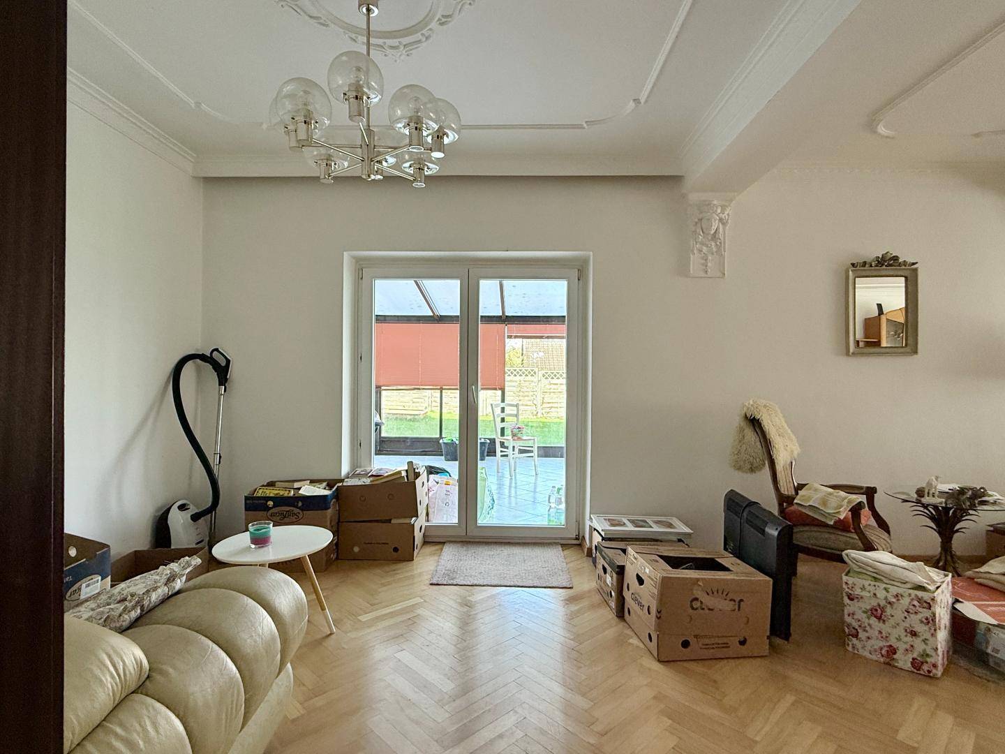 Helles Wohnzimmer mit Parkettboden, Stuckdecke und Zugang zum Wintergarten.