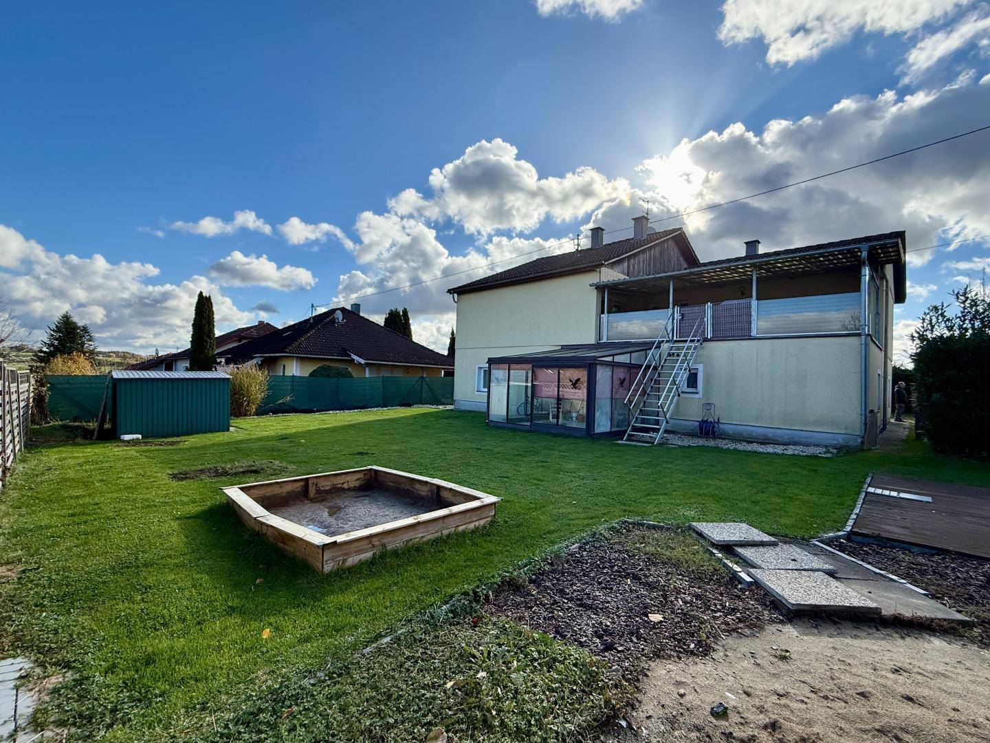 Hinterer Gartenbereich mit Rasen, Sandkasten, Geräteschuppen und Zugang zur Terrasse.