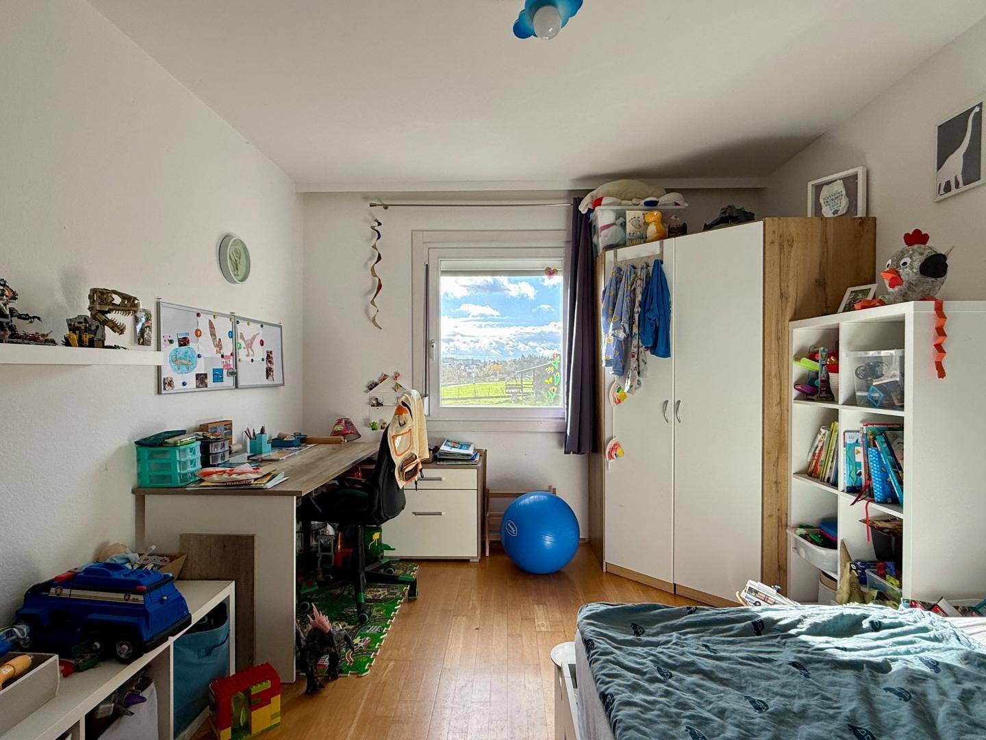 Geräumiges Kinderzimmer mit hellem Holzboden und Fenster mit Blick ins Grüne.
