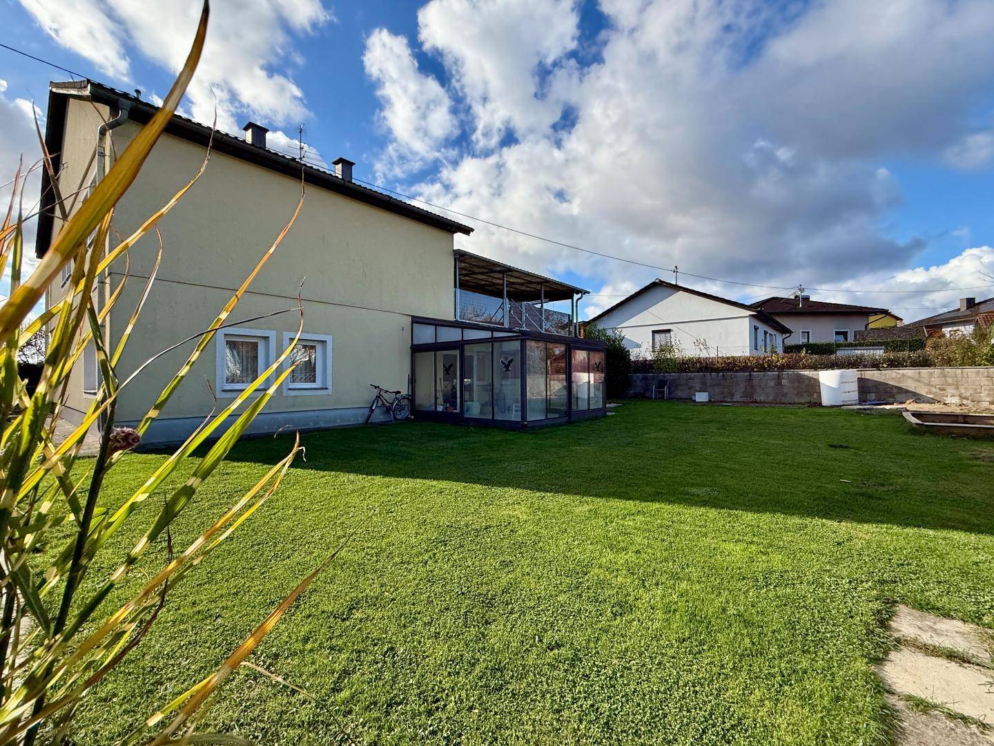 Weitläufiger Garten mit gepflegtem Rasen und einem modernen Wintergarten am Wohnhaus.