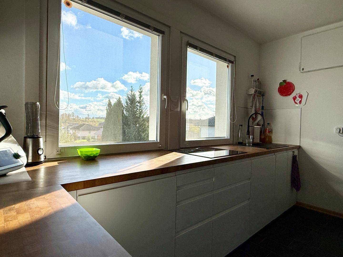 Moderne Küche mit Holz-Arbeitsplatte, weißen Unterschränken und weitem Ausblick.