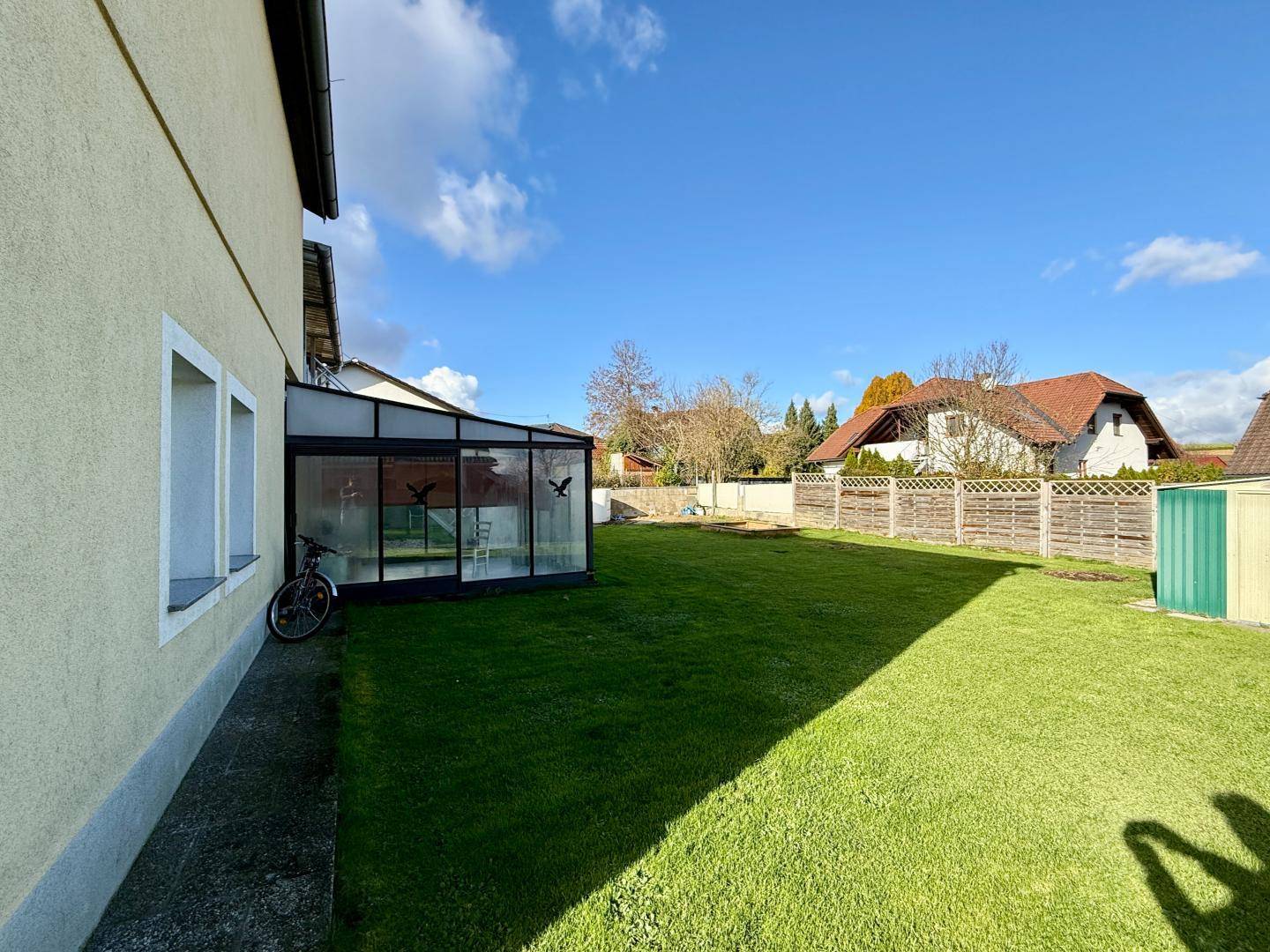 Seitlicher Gartenbereich mit Rasenfläche, Geräteschuppen und Blick auf die Nachbarschaft.