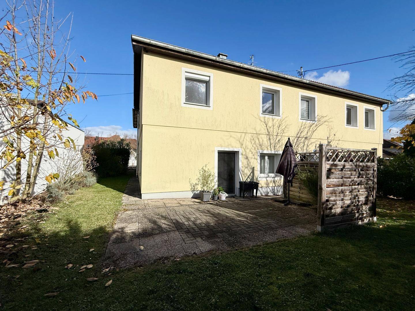 Gepflasterte Terrasse hinter dem Haus mit Sitzgelegenheiten und Zugang zum Garten.