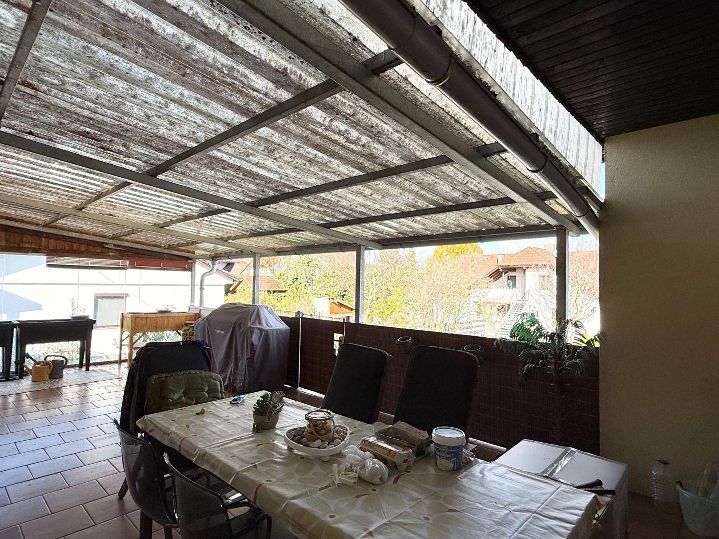 Überdachte Terrasse mit Fliesenboden und Essbereich im Freien.