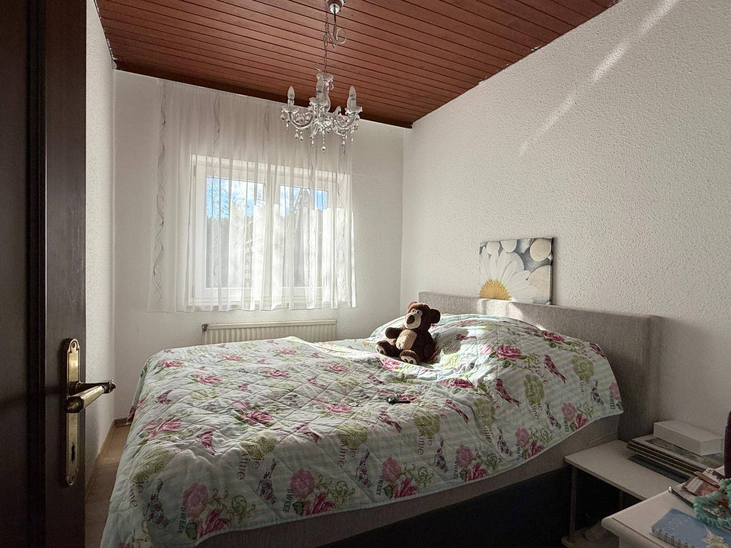 Gemütliches Schlafzimmer mit Holzbalkendecke und Fenster mit Vorhängen.