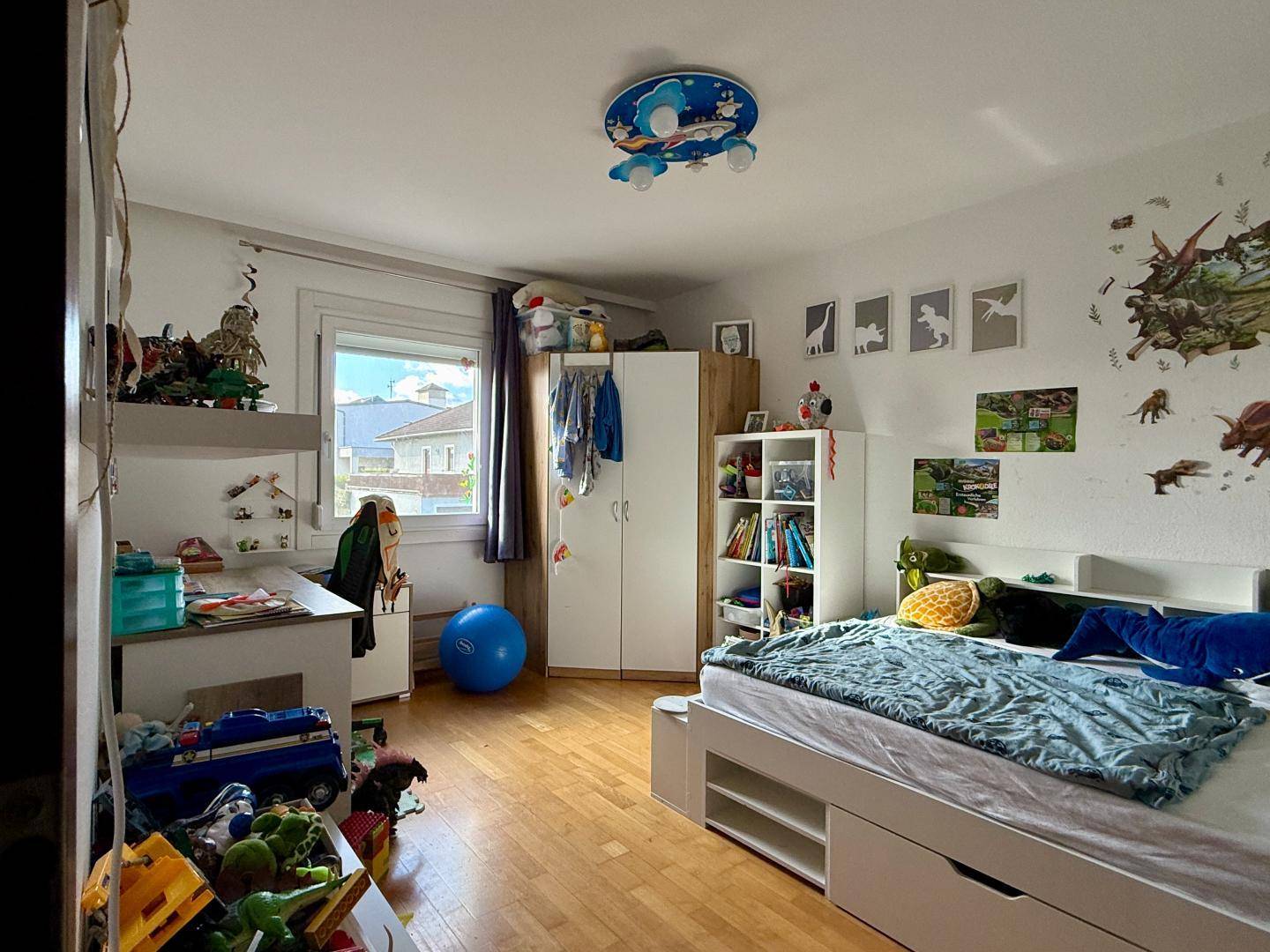 Kinderzimmer mit Holzboden, Schreibtisch und viel Stauraum für Spielzeug.