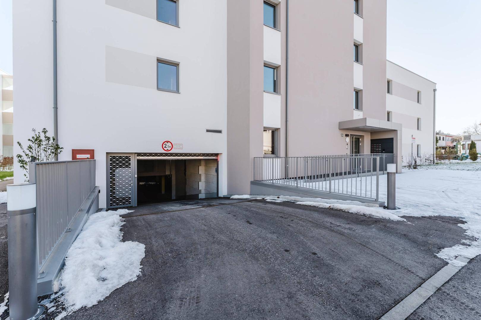 Zufahrt zur Tiefgarage eines modernen Wohngebäudes mit Rampe und Schranke.