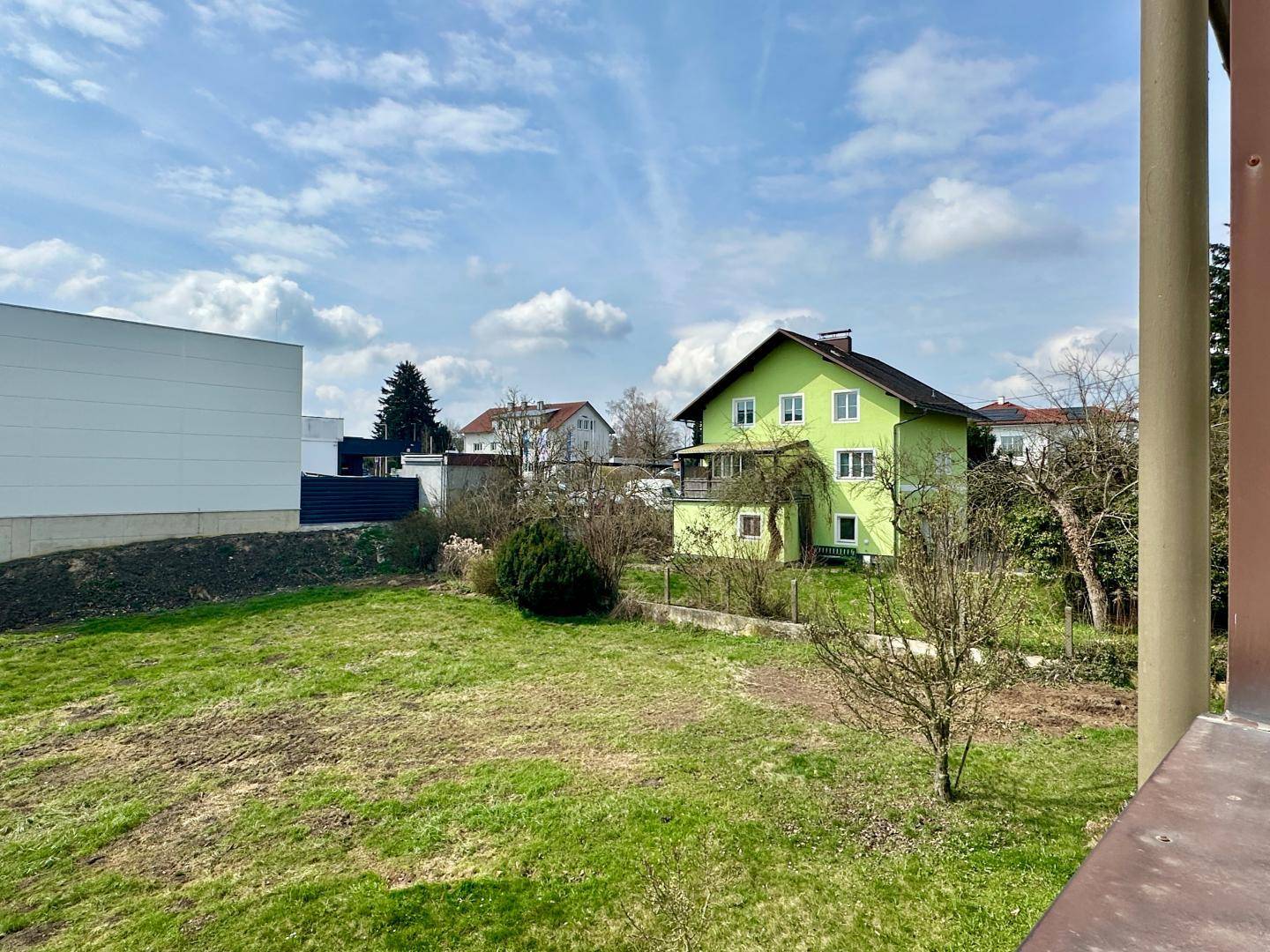 Blick aus dem Fenster auf eine grüne Rasenfläche und ein hellgrünes Nachbarhaus.