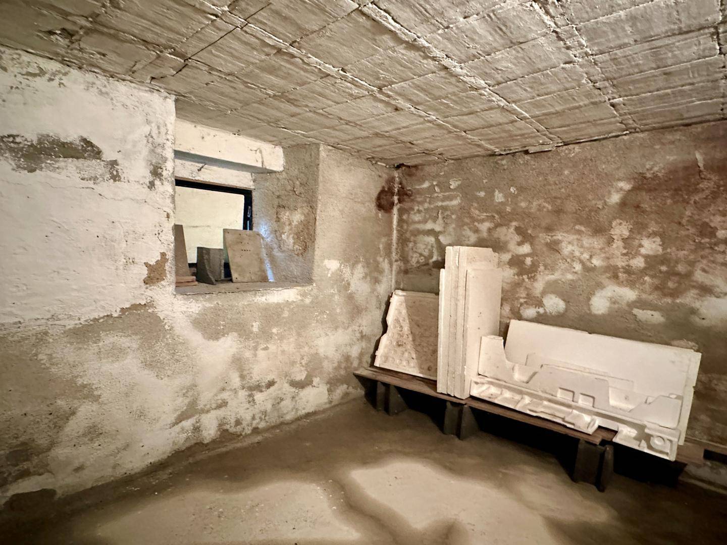 Unausgebauter Kellerraum mit rauen Wänden und kleinem Fenster.