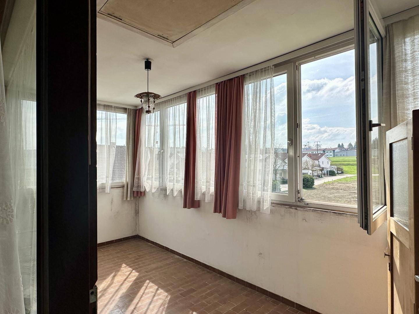 Heller, verglaster Balkon mit Fliesenboden und weitem Blick auf die Umgebung.